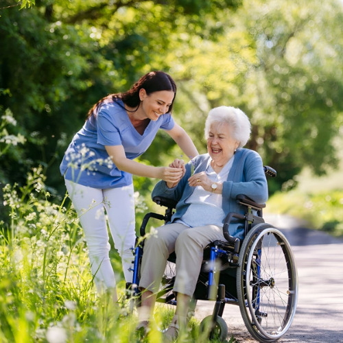 A friendly home care worker assisting a happy elderly woman in a wheelchair outdoors, representing compassionate aged care support and independence.